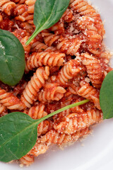 Fusilli pasta in tomato sauce in white plate. Close-up.