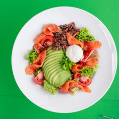 Salad with quinoa, salmon, avocado, tomatoes, lettuce and Philadelphia cheese in a white plate on a green background. Photo for the menu. Photo for clipping. Close-up