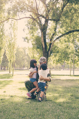 Happy dad meeting with two children after military mission trip, hugging kids on grass in park. Sunshine background. Family reunion or returning home concept