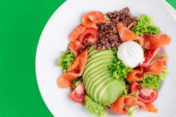 Salad with quinoa, salmon, avocado, tomatoes, lettuce and Philadelphia cheese in a white plate on a green background. Photo for the menu. Photo for clipping. Close-up