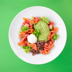 Salad with quinoa, salmon, avocado, tomatoes, lettuce and Philadelphia cheese in a white plate on a green background. Photo for the menu. Photo for clipping. Close-up