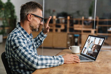 Happy grey man waving hand while taking conference call on laptop