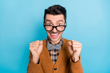 Photo of happy cheerful young guy raise fists excited win wear glasses isolated on blue color...