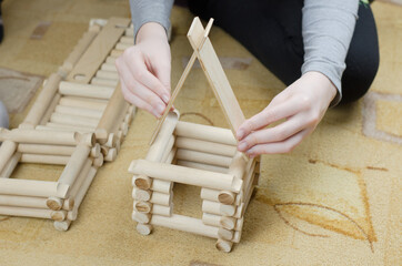Girl builds a hut from wooden logs, children's wooden constructor