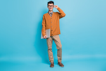 Fototapeta premium Photo of cheerful nice young guy dressed brown cardigan arm glasses holding modern device isolated blue color background