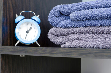 Blue alarm clock on the shelf with bath towels. Massage time
