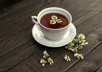 A cup of tea with chamomile on a wooden background.