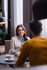 Smiling woman looking at boyfriend near dinner on blurred foreground in modern restaurant