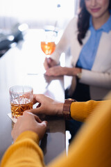 Cropped view of glass of whiskey in hand of man near friend on blurred background in restaurant
