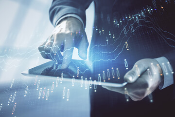 Double exposure of man's hands holding and using a digital device and forex graph drawing. Financial market concept.