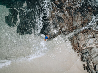 From above photo of a pretty young woman in a blue swimming suit lying on the rock in high tide. Summer vacation concept