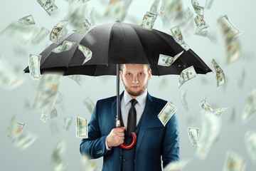 A man in a business suit with an umbrella stands against the background of falling dollars, rain of...
