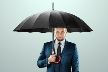 A man in a business suit stands with an umbrella in his hands on a light background. Savings and...
