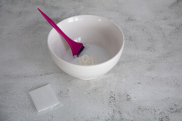 On the table is a bowl with hair dye and a brush. Home coloring concept.