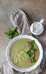 Vegetarian cream soup of green vegetables (broccoli, green peas, spinach) served with mint and seeds on concrete background. Clean eating, healthy food concept. Top view.