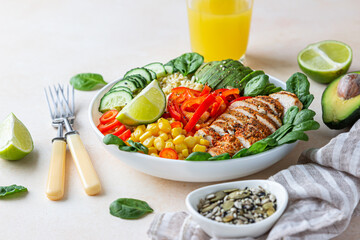 Healthy buddha bowl lunch with grilled chicken and bulgur, spinach, avocado, cucumber, bell pepper and corn on concrete background. Delicious balanced food concept.