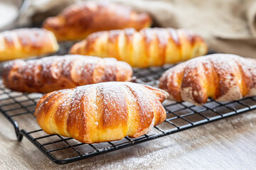 Homemade fresh yeast buns with custard filling with powdered sugar on black metal grille. Buns with vanilla cream patisier.
