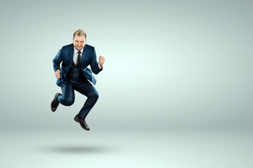 Fototapeta na wymiar A man in a business suit jumps up cheerfully against a light background. The concept of joy, success, luck, winning.