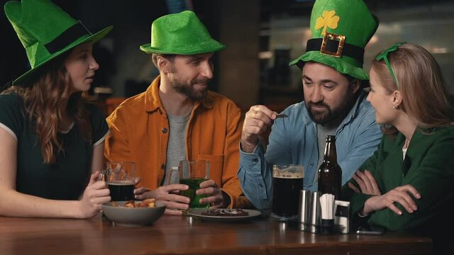 Friends in Irish hats celebrating Saint Patrick's Day in a pub. Men and women talking and having fun.
