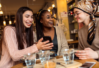Three young multi ethnic women enjoy coffee at a coffee shop.