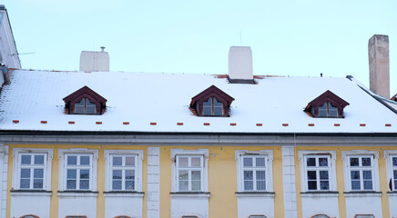 Fototapeta na wymiar Exterior of apartments with gable roofs and dormers covered with snow in winter. City building view in winter. Tiled roof in the snow. Typical European houses in Czech Republic.