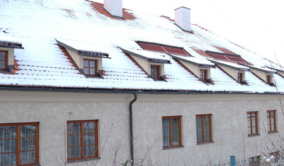Exterior of apartments with gable roofs and dormers covered with snow in winter. City building view...