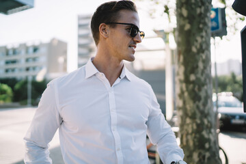 Side view of confident businessman in stylish sunglasses looking away during working daytime in financial district, Caucasian male boss 30s in trendy wear standing at metropolitan city street