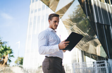 Fototapeta premium Handsome male employer using digital tablet during work break in financial district, Caucasian businessman reading received email message at modern technology connecting to 4g internet in city