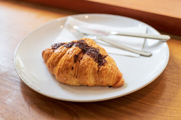 French chocolate croissant on plate on wooden table and nature sunlight with shadow through from window