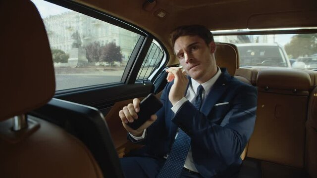 Joyful Businessman Dancing With Mobile Phone In Interior Of Business Car.