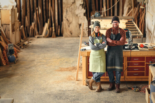 Positive carpentry workshop owners standing near workbench