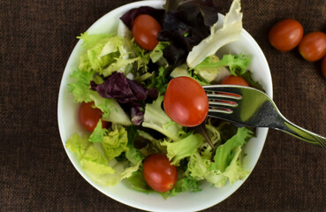 Close up, picking a cherry tomato with the fork, from the white bowl, with variety of salad.