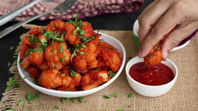 Hand dipping Gobi Manchurian dry sauce Gobi 65 popular Indian street food snack Delhi Mumbai India cauliflower florets Veg Manchurian chilly gobi 4K slow motion footage video Indo Chinese side dish  