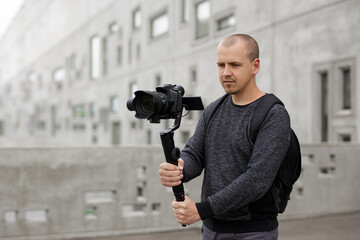 hobby and creativity concept - professional videographer shooting video using modern dslr camera on 3-axis gimbal over grey concrete wall background