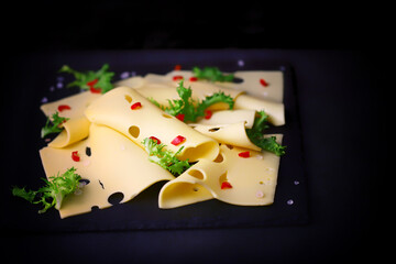 Slices of cheese with spices on a black background.