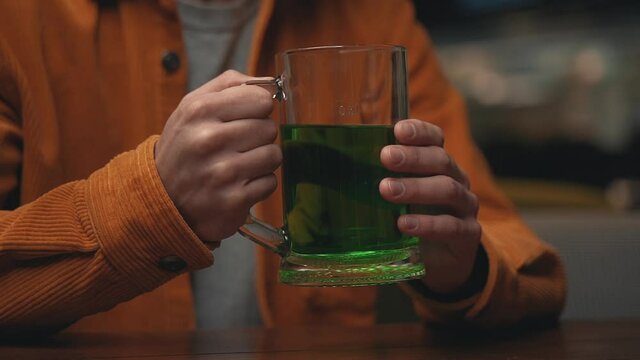 Holding a green beer mug. Close-up. Celebrating Saint Patrick's Day in a pub. 