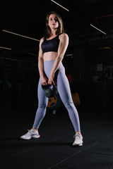 Fototapeta na wymiar Young woman with athletic body poses standing in the gym with kettlebell.