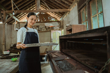 the girl in an apron carries a baking sheet of cake batter to put in the already lit oven with the kitchen in the background