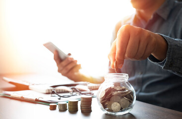 Businessman handing and putting coin in glass bottle bank with money stack step up growth. Planning...