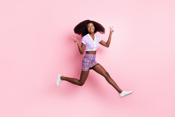 Fototapeta na wymiar Full length body size view of beautiful trendy cheerful girl running jumping showing v-sign isolated over pink pastel color background
