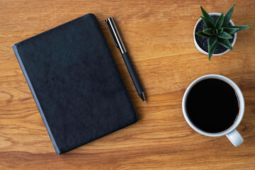 Top view of black closed cover blank notebook with coffee cup and pen for taking write notes on wood table background. Flat lay, creative workspace office. Business-education concept with copy space.