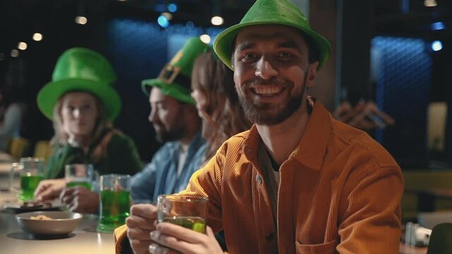 Portrait of smiling happy man looking at camera with a mug of beer. Friends celebrating Saint Patrick's Day in a pub.