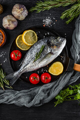Raw dorado fish and spices for cooking it in a frying pan on a black background, top view vertical photo