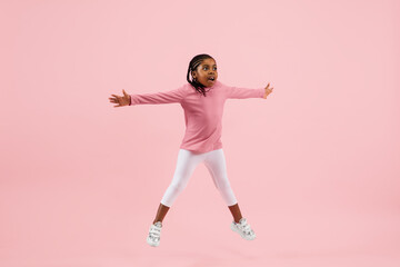 Jumping, flying. Childhood and dream about big and famous future. Pretty little girl isolated on coral pink studio background. Dreams, imagination, education, facial expression, emotions concept.