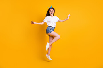 Fototapeta na wymiar Full length body size photo of cheerful girl jumping high wearing jeans shorts white t-shirt headband on bright yellow color background