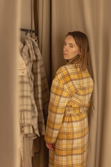Fototapeta premium Woman trying on a coat in a fitting room of a clothing store