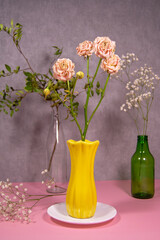 Obraz premium Dried rose in a yellow vase on a white saucer. Pistachio branch in a transparent bottle, gypsophila in a green bottle. Gypsophila lies below. Natural eco concept