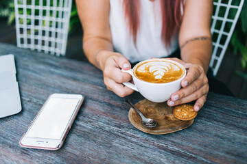 Young hipster woman drinking cappuccino while sitting at cafe