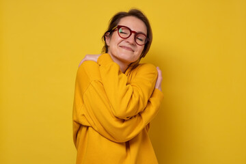 woman closing eyes in enjoyment, hugging herself, feeling comfortable and cozy, embracing herself