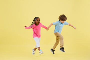 Jumping high. Childhood and dream about big and famous future. Pretty little kids isolated on yellow studio background. Dreams, imagination, education, facial expression, emotions concept.